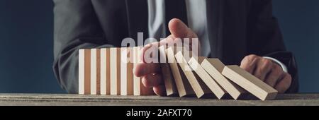 Wide view image of business crisis manager stopping wooden dominos from collapsing in a conceptual image of management and decision making. Stock Photo
