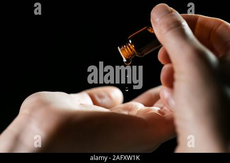 skin care and treatment - woman pouring oil in a hand from vial on black background Stock Photo