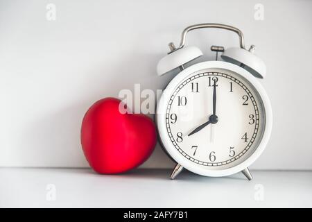 Love times memory concept. Retro white bell clock with red heart on white wall space for text. Stock Photo