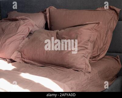 Four crumpled pillows and a sheet on bed and the sun is shining on them Stock Photo
