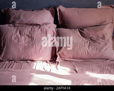 Four crumpled pillows and a sheet on bed and the sun is shining on them Stock Photo