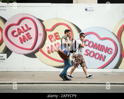 Love Hearts: Call Me. Pedestrians on mobile phones walking by advertising for Love Hearts, a UK sweet brand, with the slogan 'Call Me'. Stock Photo