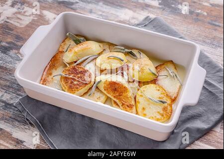 Closeup baked sliced potato with red onion and herbs: sage, rosemary and thyme in a ceramic baking dish. Stock Photo