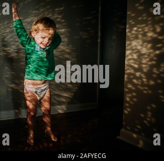 toddler stretching up in reflection of sunlight in hallway Stock Photo