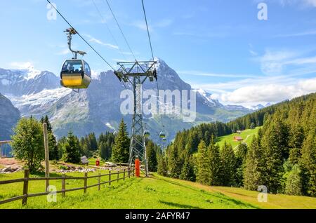 Yellow cable car in the Swiss Alps. Gondola going from Grindelwald to First in the Jungfrau area. Summer Alpine landscape with snowcapped mountains in the background. Transport tourists uphill. Stock Photo