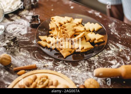 Cooking Christmas cookies at home on the wooden table. Plate with freshly baked cookies in the shape of Christmas trees Stock Photo