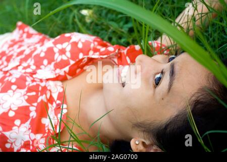 Close up portrait of happy Southeast Asian young woman laying on green grass seems to enjoy a beautiful day in nature. Stock Photo