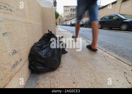 Black garbage bags placed on sidewalk for waste collection in Malta Stock Photo