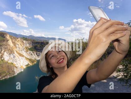 Asian female tourists are taking pictures of themselves at tourist attractions using a smartphone. Stock Photo