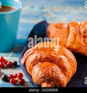 French breakfast: Ruddy croissants with forest berries and a cup of coffee with milk stand on a table Stock Photo