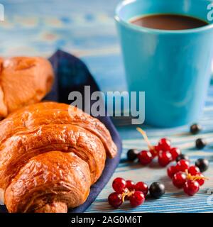 French breakfast: Ruddy croissants with forest berries and a cup of coffee with milk stand on a table Stock Photo