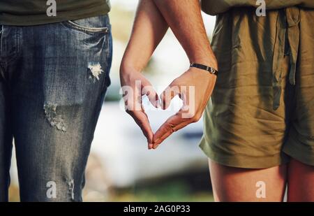 Making heart and love gesture by the hands. Young couple have a good time in the forest at daytime Stock Photo