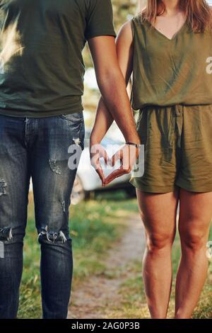 Making heart and love gesture by the hands. Young couple have a good time in the forest at daytime Stock Photo