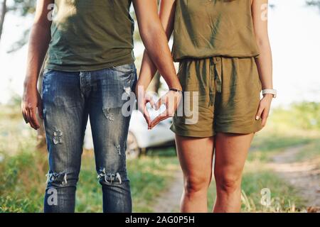 Making heart and love gesture by the hands. Young couple have a good time in the forest at daytime Stock Photo