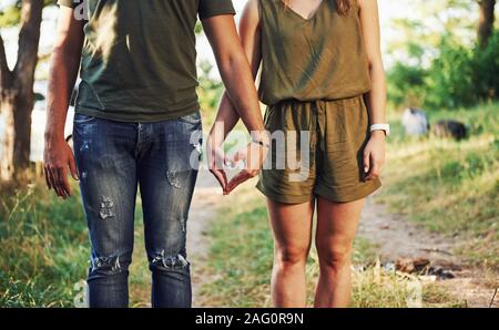 Making heart and love gesture by the hands. Young couple have a good time in the forest at daytime Stock Photo