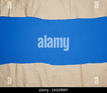 torn brown sheet of paper on a blue background, full frame, close up Stock Photo