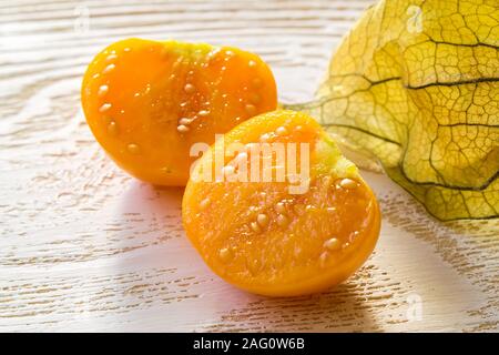 Close-up of cut in half yellow physalis fruit (Physalis peruviana) in the sunshine on a white wooden table. Fruits and vegetables, vegetarianism. Stock Photo