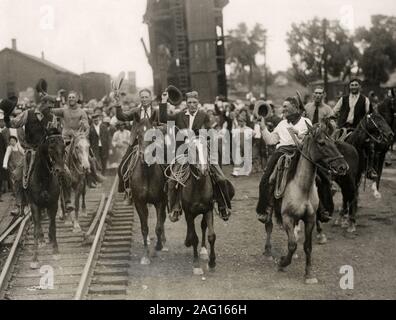 Early 20th century vintage press photograph - cheering cowboys ride along railway track on horses, USA circa 1920s. Miles City Montana Stock Photo