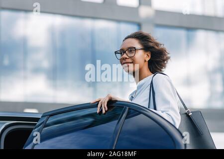 Young businesswoman getting into a taxi. Beautiful female standing at car outdoors. Stock Photo