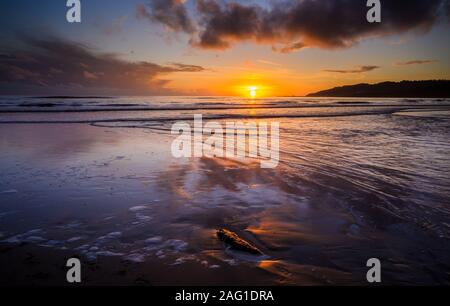 Charmouth,  Dorset, UK. 17th December 2019. UK Weather: Beautiful colours in the sky at sunset are reflected in the wet sand at low tide as the sun sets over the horizon near Charmouth at the end of a winter's day.   Credit: Celia McMahon/Alamy Live News.