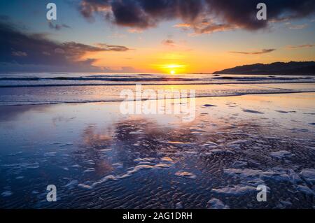 Charmouth,  Dorset, UK. 17th December 2019. UK Weather: Beautiful colours in the sky at sunset are reflected in the wet sand at low tide as the sun sets over the horizon near Charmouth at the end of a winter's day.   Credit: Celia McMahon/Alamy Live News.