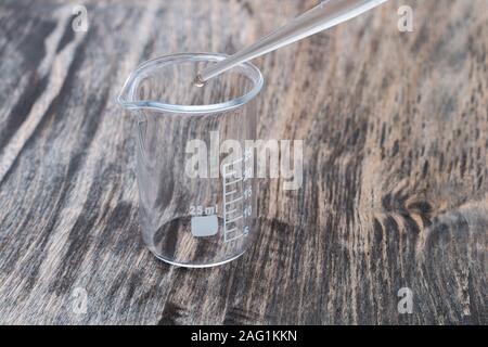 Close-up side view of 25 ml chemistry empty measuring beaker with a pipette on the wooden surface Stock Photo