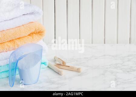 Blue plastic measuring beaker with detergent, stack of white terry towels and wooden clothespins are on a marble surface against a white background of Stock Photo