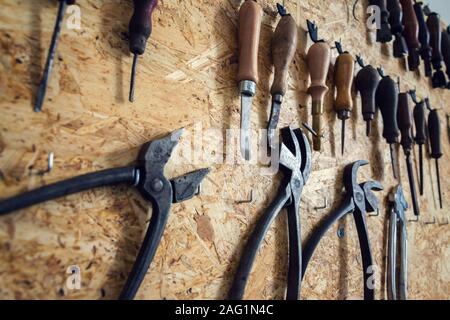 Group of old cobblers tools for handmade shoes production, awls and tongs for leather on wooden chipboard background Stock Photo