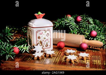 Christmas scene with cinnamon stars, rolling pin, a ceramic biscuit tin and other christmas decoration on an old wooden table. Stock Photo