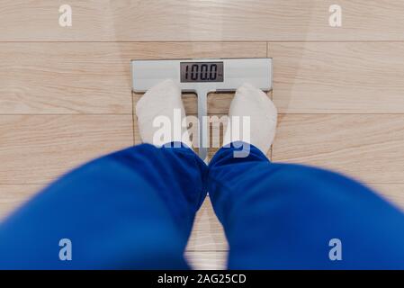 A man weighing himself on a digital scale dressed in blue pajamas and white socks. Problem overweight. Diet concept. Stock Photo