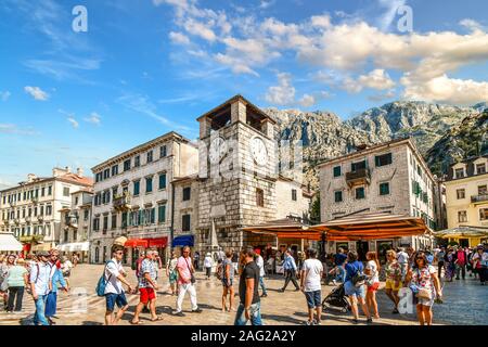 Tourists sightsee, dine at cafes and shop under the clock tower in the Square of the Arms, in the medieval walled city of Kotor, Montenegro Stock Photo