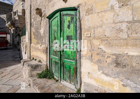 A brilliant, bright green, weathered wooden doorway into a stone building in the ancient city of Matera, Italy, in the Basilicata region. Stock Photo