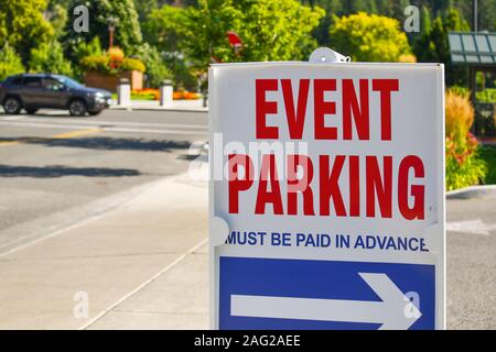 A red, white and blue parking sign on a street sidewalk points towards event parking on a sunny day in a non-descript mountain town. Stock Photo