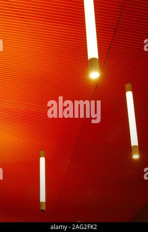 Intense orange ceiling with vertical light tubes. Modern architecture, interior. Stock Photo