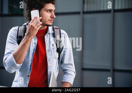 Young adult man talking on modern smartphone at street Stock Photo