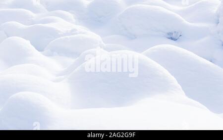 Soft, round shapes of snow-covered rocks along a riverbank in the winter.