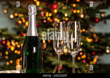 A bottle of champagne and two empty glasses stand in the background of the Christmas tree Stock Photo
