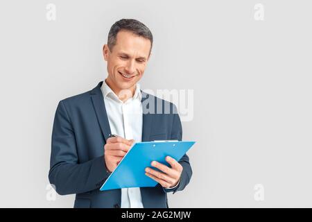 Freestyle. Mature businessman standing isolated on white with clipboard taking notes happy Stock Photo