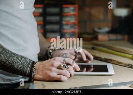 Craftsman artist using a tablet and checking some ideas for a new designer wooden product in his home workshop while smoking a cigarette Stock Photo