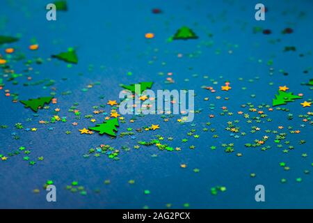 Christmas frame composition with golden star-shaped sequins and pine trees on blue holographic background. Celebration preparation concept. Selective Stock Photo
