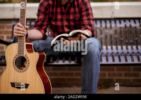 A closeup shot of a male sitting white holding the guitar and reading a book with a blurred background Stock Photo