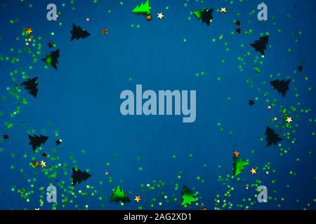 Christmas frame composition with golden star-shaped sequins and pine trees on blue holographic background. Celebration preparation concept. Selective Stock Photo