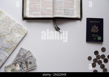 Overhead shot of an open bible with passport, map, and dollar bills on a white surface Stock Photo