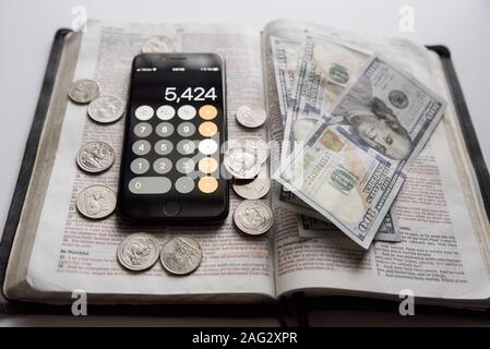 High angle shot of an open bible with dollar bills and smartphone on top Stock Photo