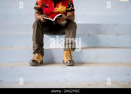 Person sitting on the stairs while reading the bible Stock Photo