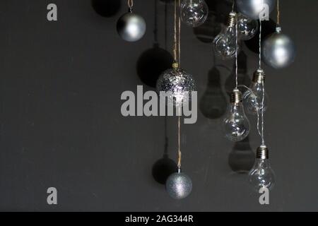 New Year or Christmas background, close-up of silver christmas bubbles and garland of light bulbs on a dark backdrop, selective focus Stock Photo