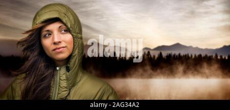 Woman wearing winter jacket, in front of misty forest landscape. Stock Photo