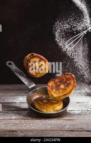 Pancakes and frying pan levitate over a table, and on top a whisk and sprinkled with flour Stock Photo