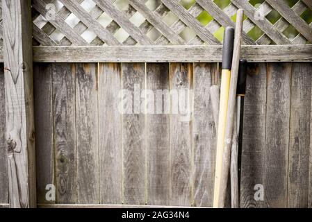 Closeup shot of leaf rake and shovel handle leaned again a wooden fence in the backyard Stock Photo