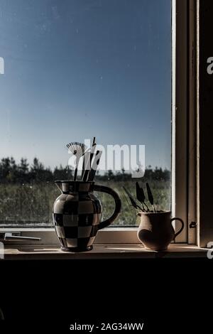 Vertical shot of two vases near the window filled with art supplies with the background of daylight Stock Photo